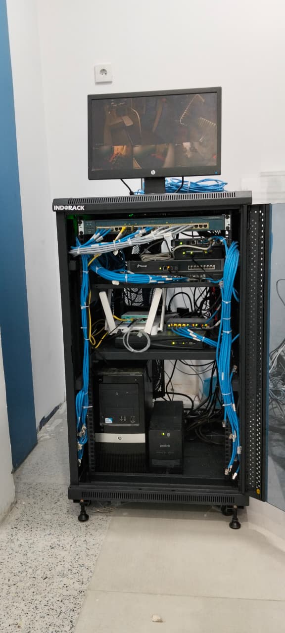 Rak baja terbuka dengan patch cord menggantung sampai ke lantai, dipindahkan ke kabinet 19 inci dengan jalur kabel yang ditata ulang. — Sesudah
